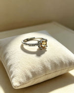 Silver ring with a yellow gemstone on a white cushion