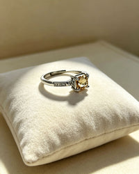 Silver ring with a yellow gemstone on a white cushion