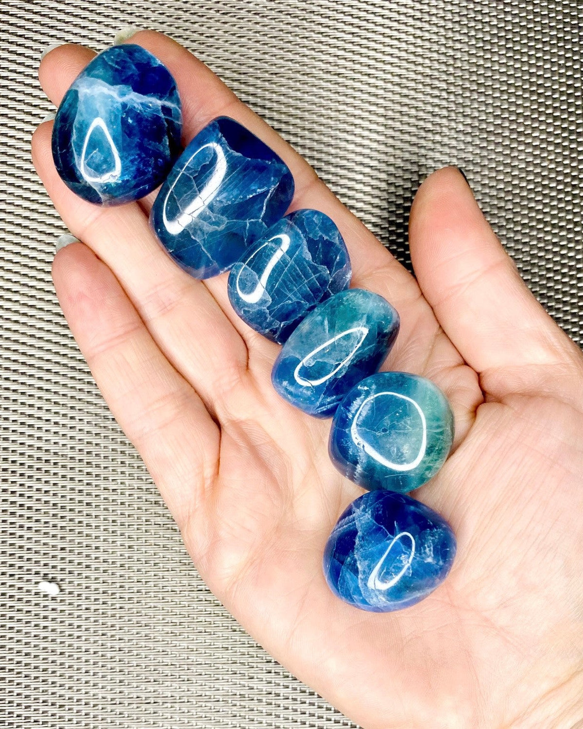 A person's hand holding multiple tumbled stones with a deep blue color and patterns.