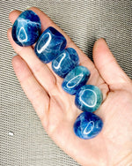 A person's hand holding multiple tumbled stones with a deep blue color and patterns.