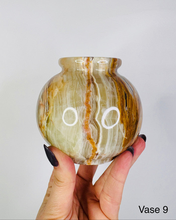 A hand holding a conical shaped green onyx vase with a marbled pattern.