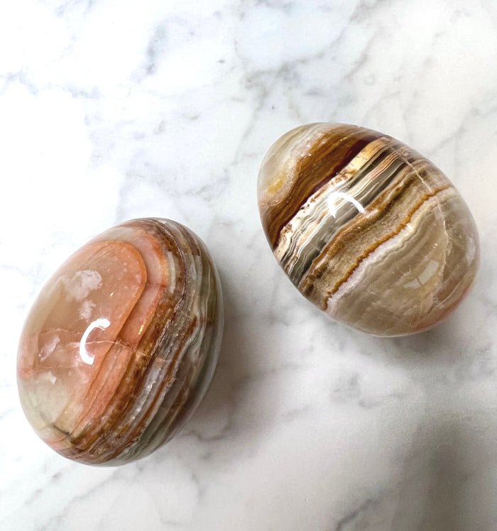 Two polished green onyx eggs with unique colour banding on a marble background.